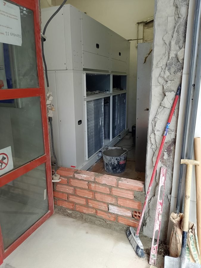Máquina de climatización introducida por el hueco abierto en fachada, con el murete de ladrillo en ejecución